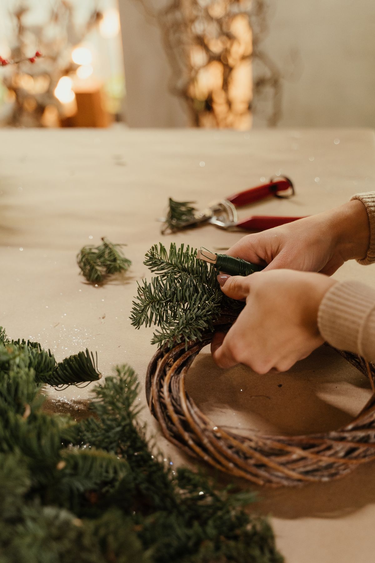 Hands crafting a holiday wreath on a wooden table